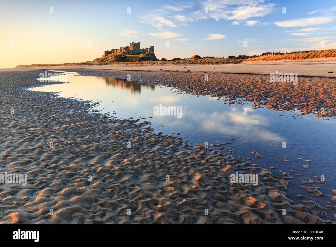 Il castello di Bamburgh riflessa in un pool di marea in inizio di mattina di sole. Foto Stock