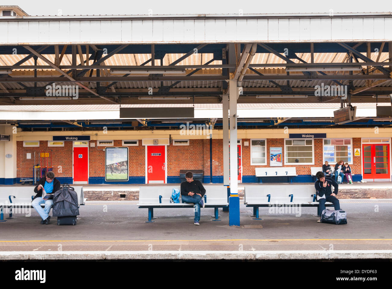 I passeggeri sulla piattaforma panche in attesa alla stazione di Woking. Foto Stock