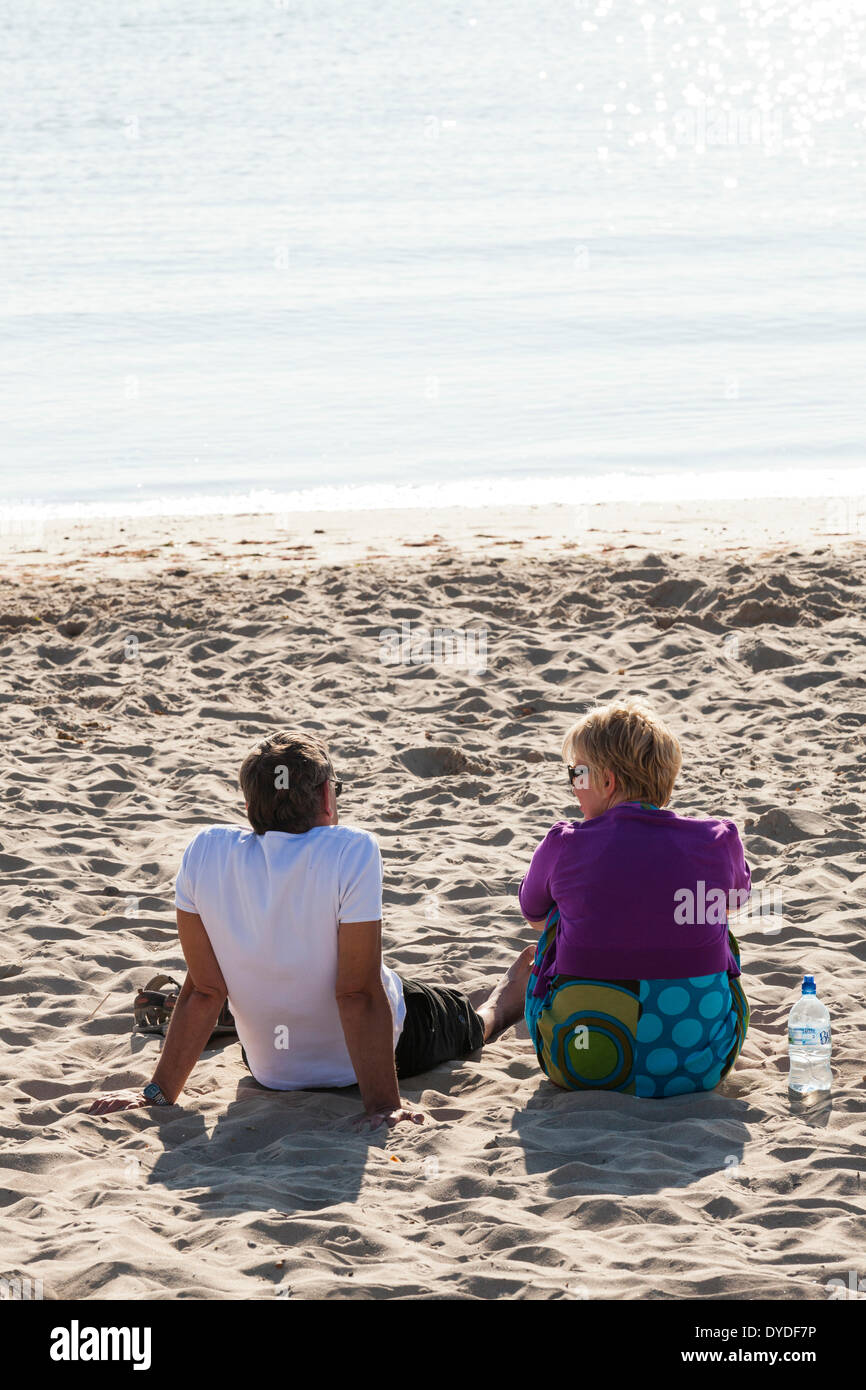 Giovane seduto da solo su una spiaggia di sabbia godendo di mattina presto la luce del sole. Foto Stock