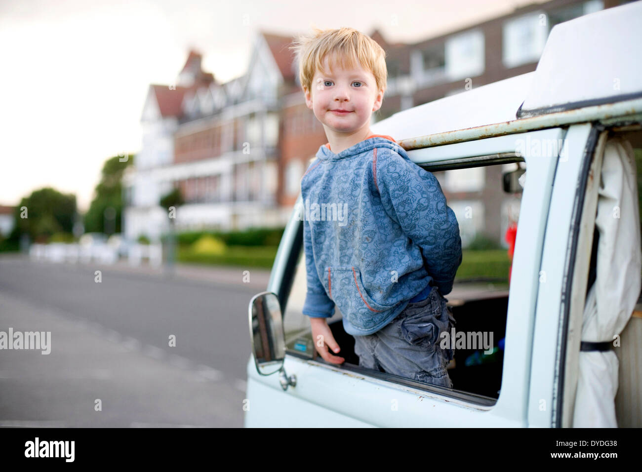Un giovane ragazzo guarda fuori del suo bus VW a lato del mare. Foto Stock