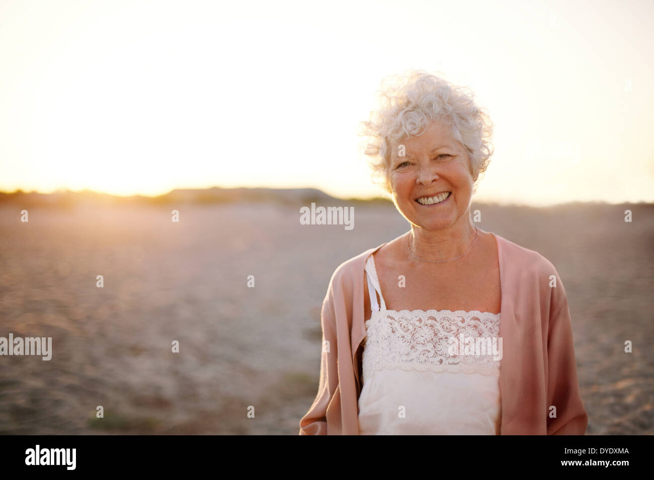 Ritratto di Allegro vecchia donna in piedi sulla spiaggia. Sorridente senior femmina caucasica sorridente all'esterno. Foto Stock