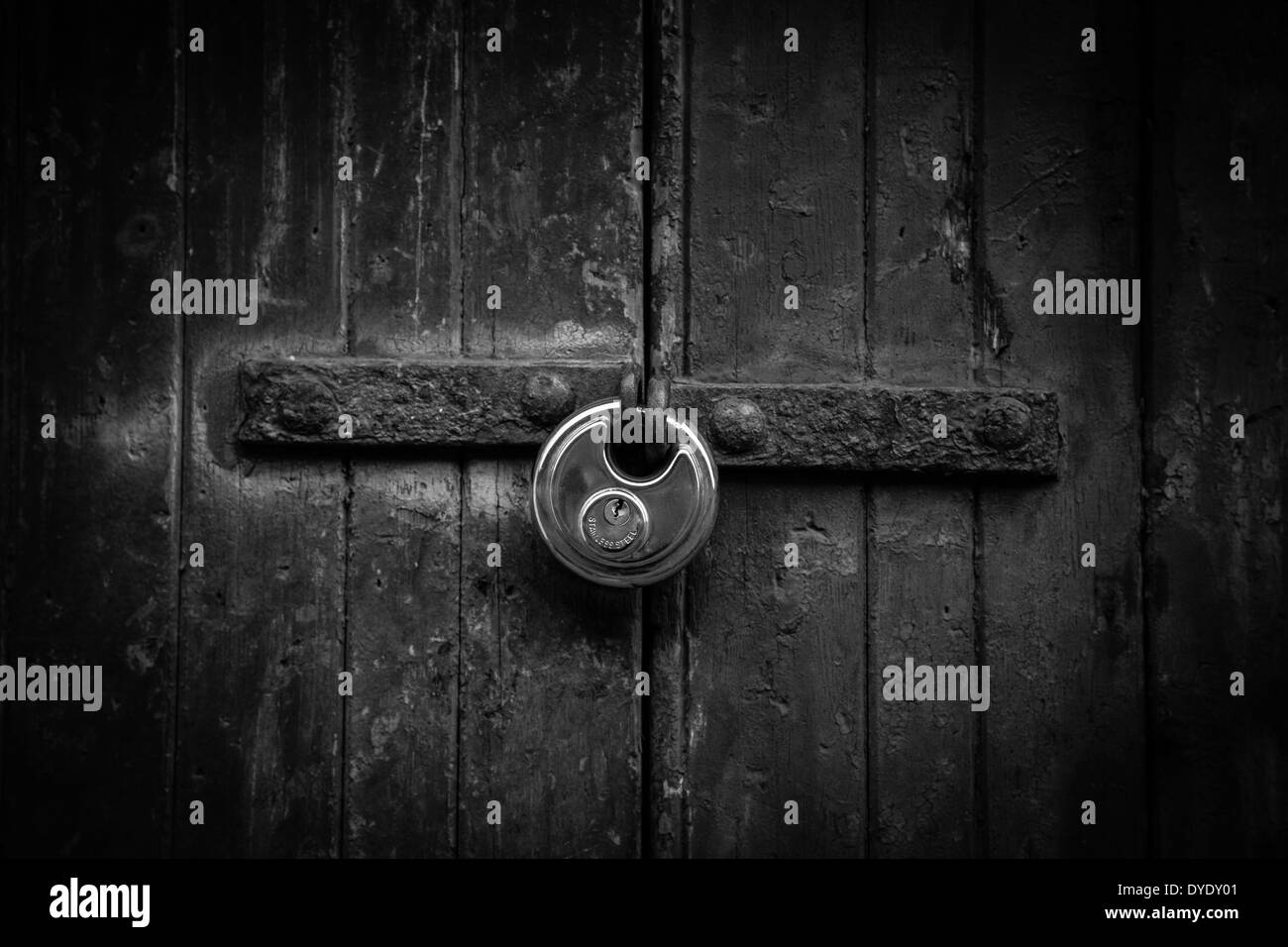 Lucchetto in acciaio su una vecchia porta di legno (B&W). Foto Stock