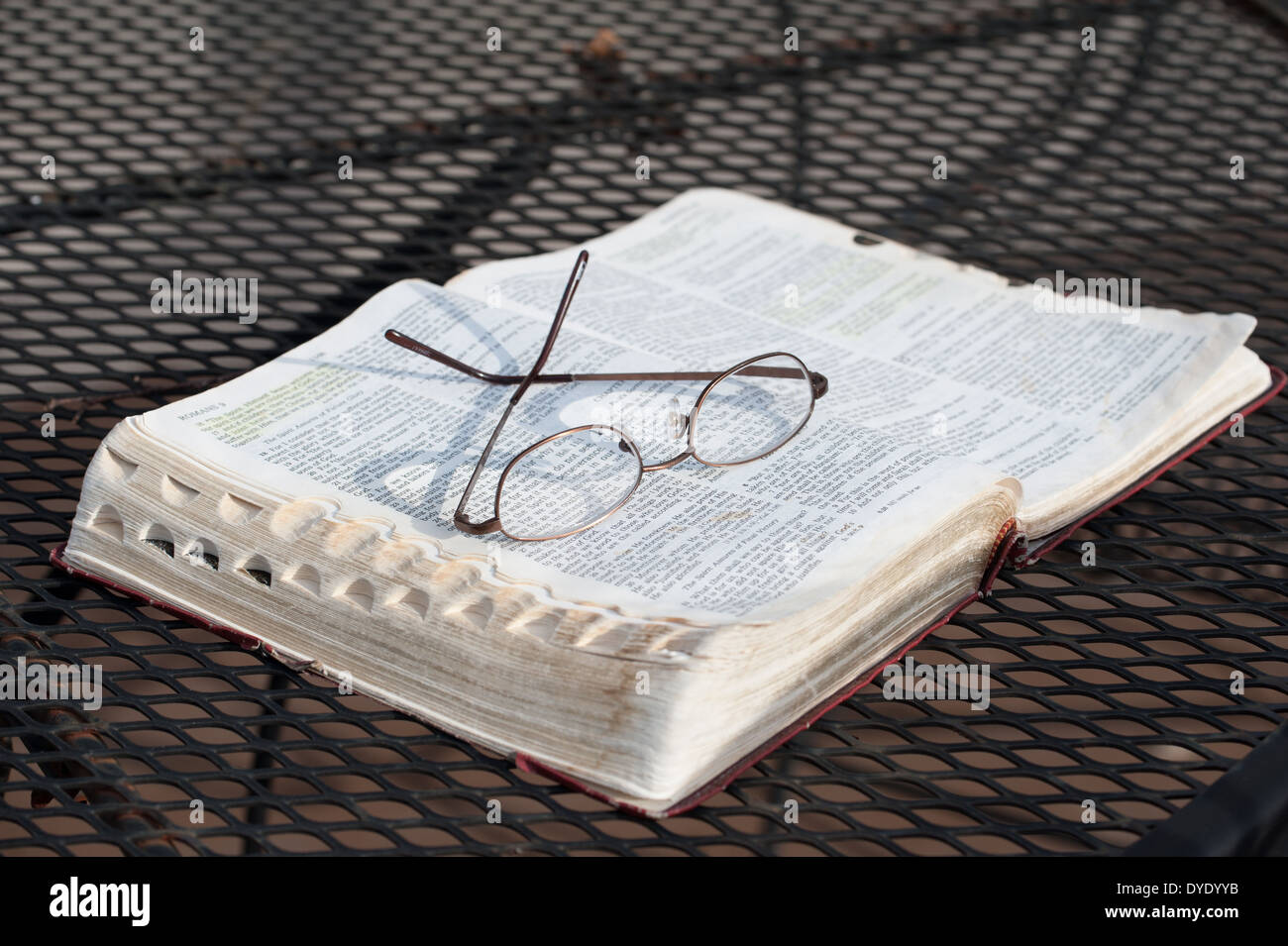 Un primo piano di un paio di occhiali per leggere in appoggio sulla parte superiore di un usurato, aprire la Bibbia su un ferro battuto patio tabella Foto Stock