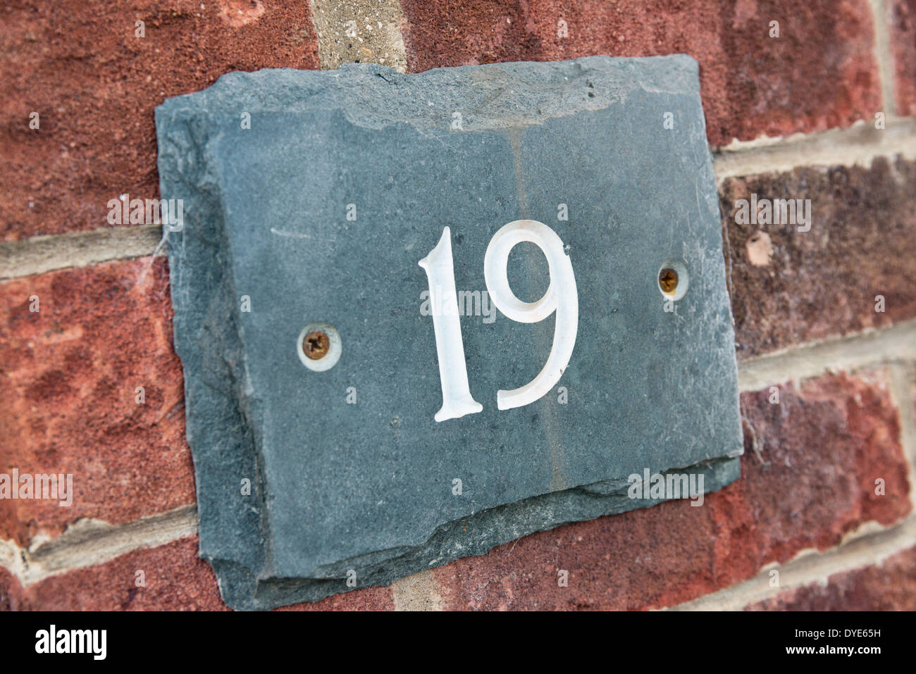 Il numero 19 sul grigio di una placca di ardesia scolpita in numeri bianchi avvitato ad una punta di rosso la parete in mattoni a significare la casa del discorso Foto Stock