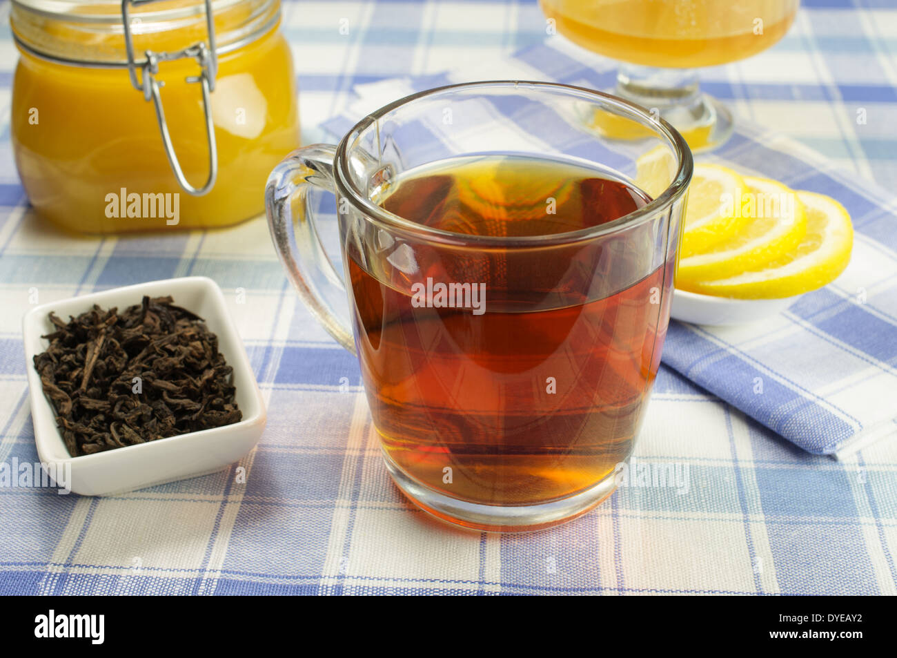 Tazza di tè con un vasetto di miele e le fette di limone sulla tavola. Ciotola con foglie di tè al di fuori. Foto Stock