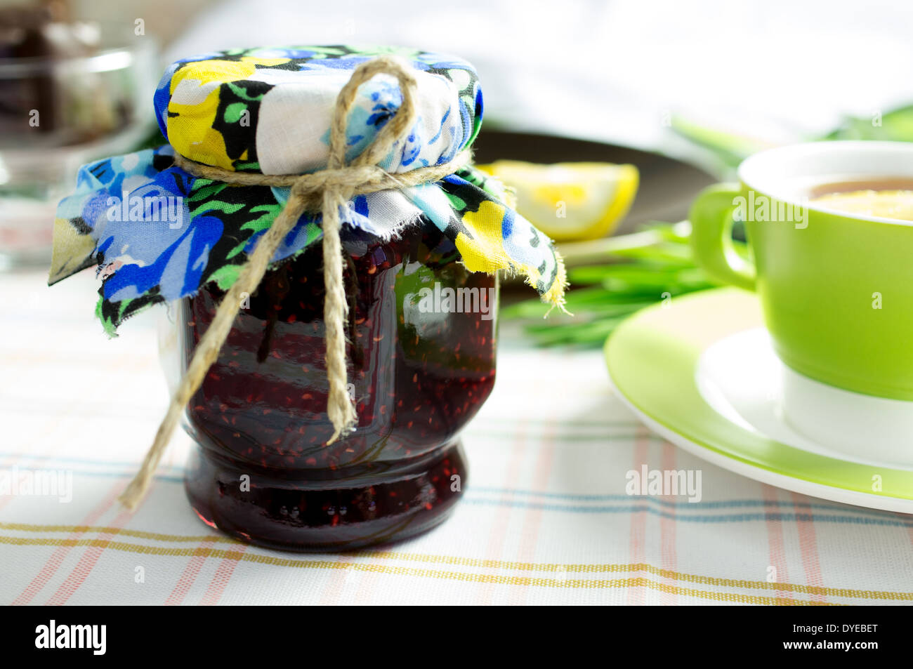 Marmellata fatta in casa, confettura di lamponi in un vasetto di vetro. Bollitore per tè e cioccolatini sul tavolo. Foto Stock