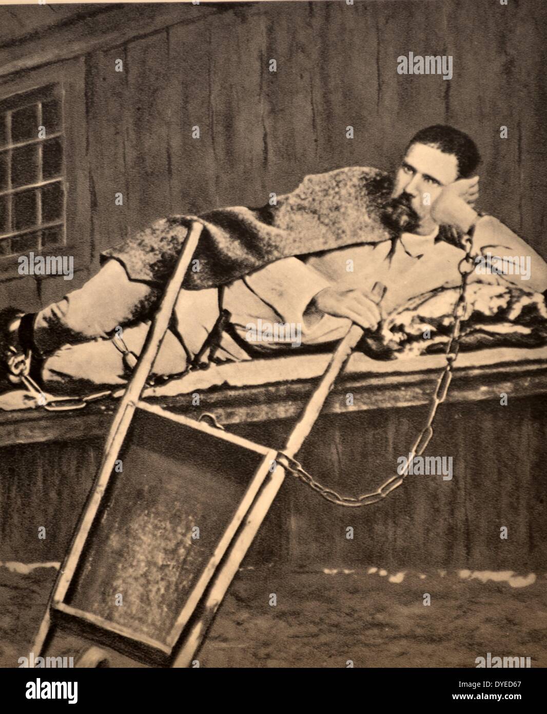 Una fotografia di un prigioniero maschio in appoggio mentre incatenato ad una carriola. Datata 1908. Foto Stock