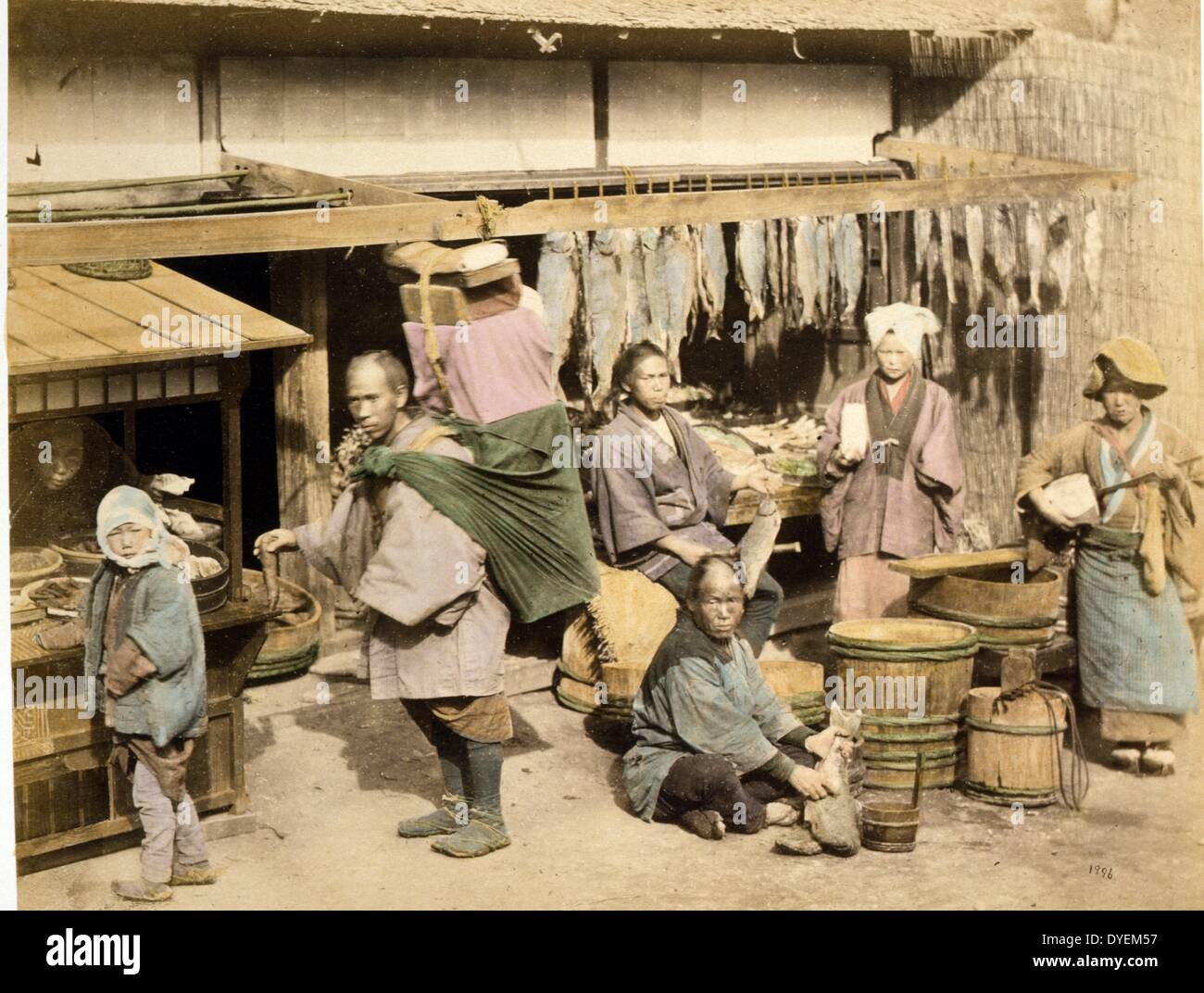 Vista esterna di un giapponese al mercato del pesce con diverse persone, acquirenti e merchant, tenendo pesce, anche un facchino con pacchetto grande sulla schiena e una donna che gioca a shamisen. 1877. Stampa fotografica, colorate a mano con acquerello Foto Stock