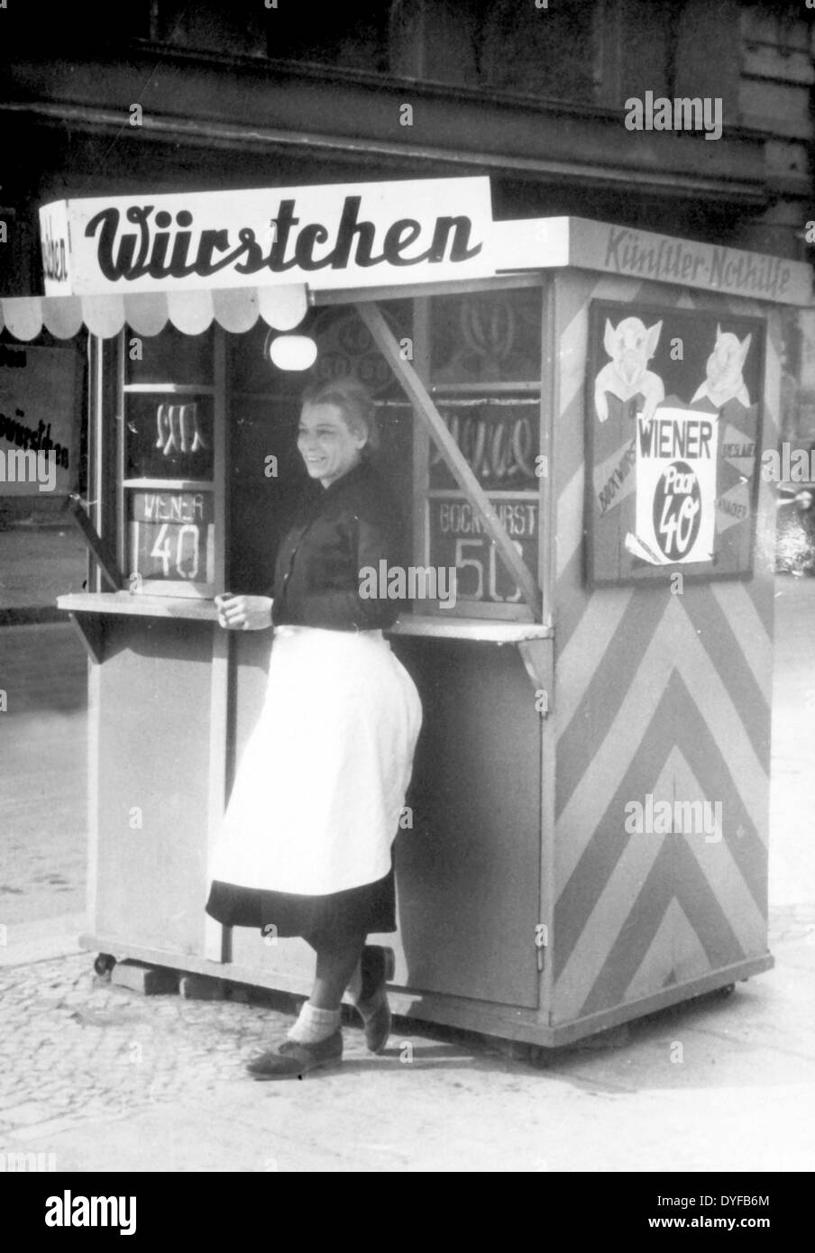 Un artista che lavora come venditore vende salsicce in uno stand d'emergenza dell'artista all'angolo tra Kurfuerstendamm e Fasanenstrasse a Berlino nel 1950. Fotoarchiv für ZeitgeschichteGrohs - SENZA FILI Foto Stock