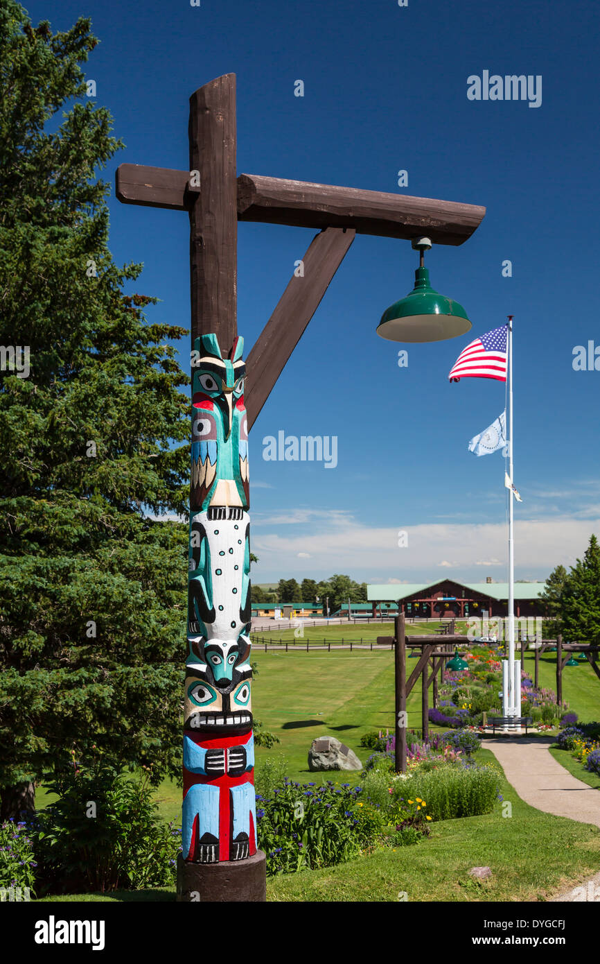 Un totem pole con bandiere e giardino fiorito presso il Glacier Park Lodge nel ghiacciaio est, Montana, USA. Foto Stock