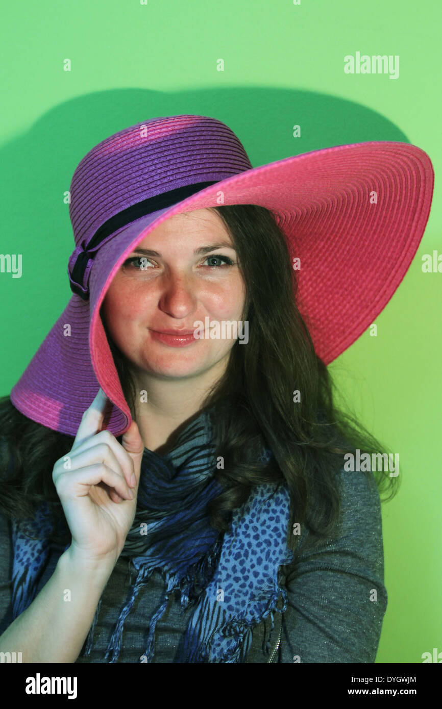 Ritratto di una giovane donna con pinky cappello di paglia su sfondo verde. Foto Stock
