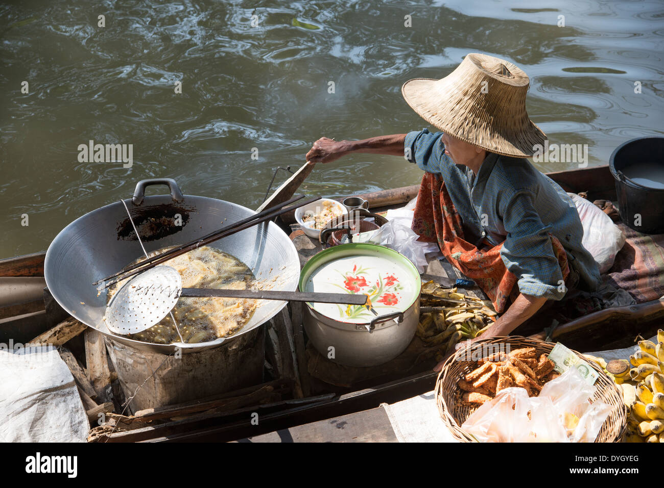 La donna nel cappello di paglia di vendita di alimenti dalla sua barca al Mercato Galleggiante di Damnoen Saduak vicino a Bangkok in Tailandia Foto Stock