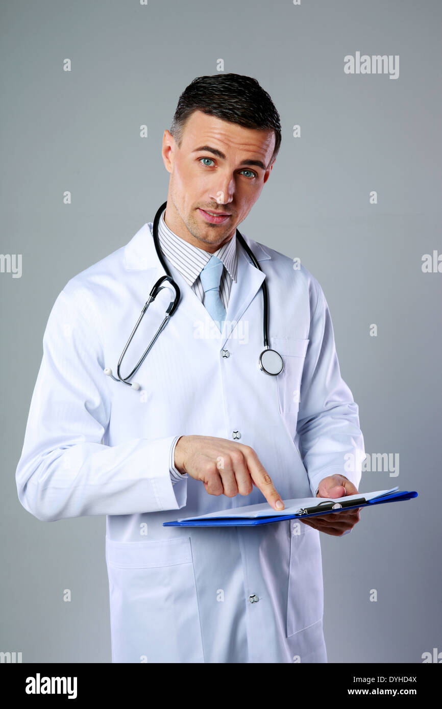 Medico maschio raccontando la diagnosi e la mostra su appunti su sfondo grigio Foto Stock