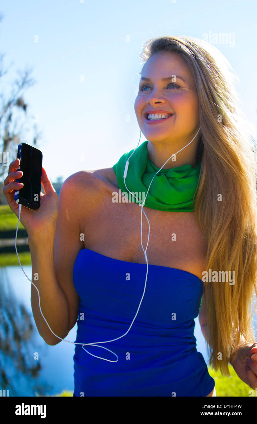 Bella bionda donna di mezza età in ascolto di musica su iPhone LETTORE MP3 con cuffie Foto Stock