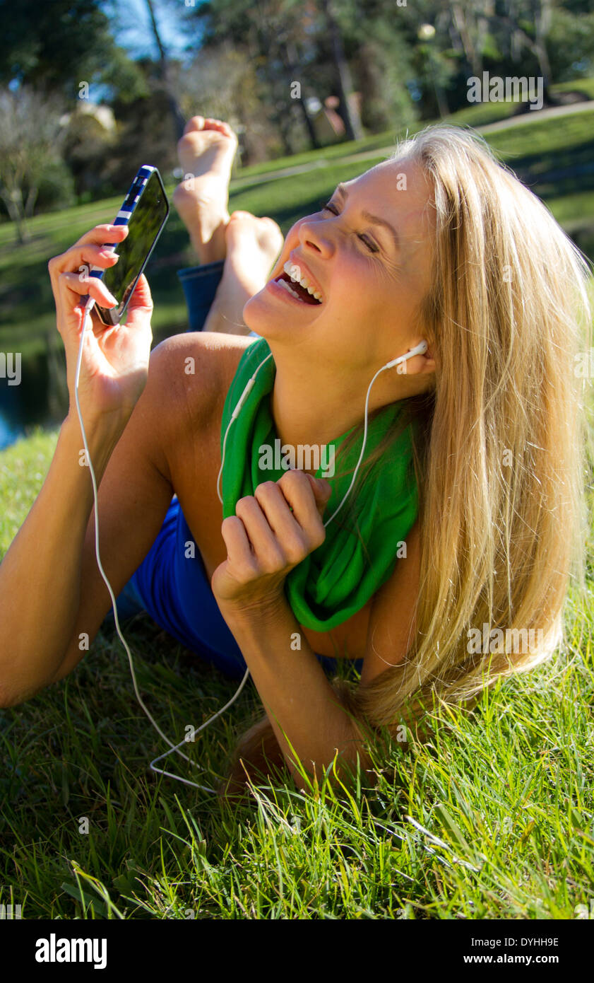 Bella bionda donna di mezza età in ascolto di musica su iPhone LETTORE MP3 con cuffie Foto Stock