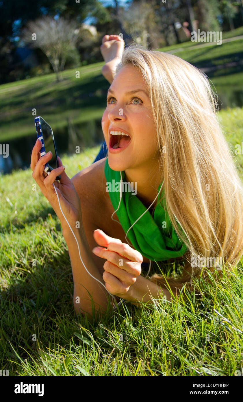 Bella bionda donna di mezza età in ascolto di musica su iPhone LETTORE MP3 con cuffie Foto Stock