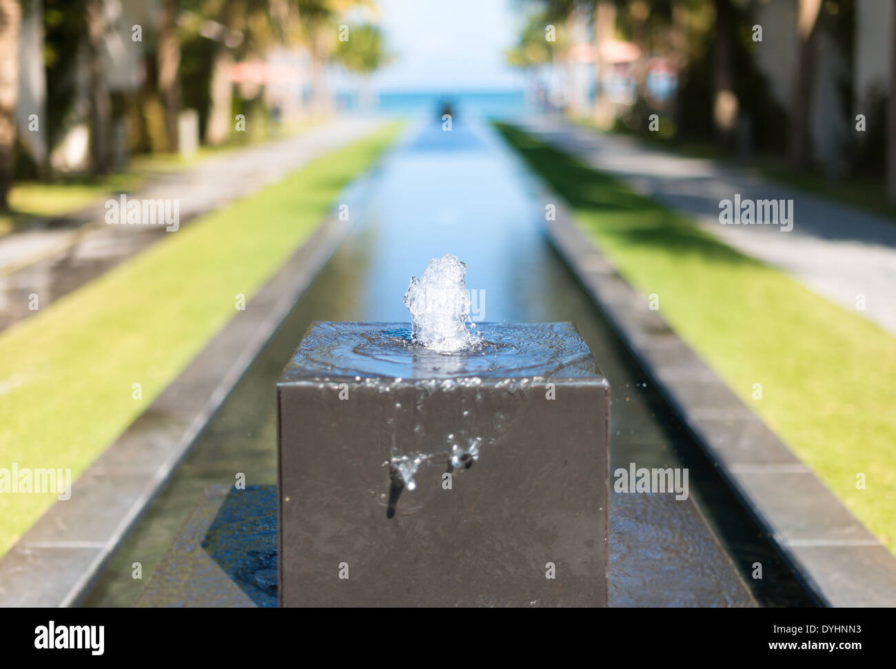 Dettaglio dell'area hotel decorazione: piccola fontana di pietra di forma cubica. Linea di acqua, prati verdi e strade con alberi in background Foto Stock