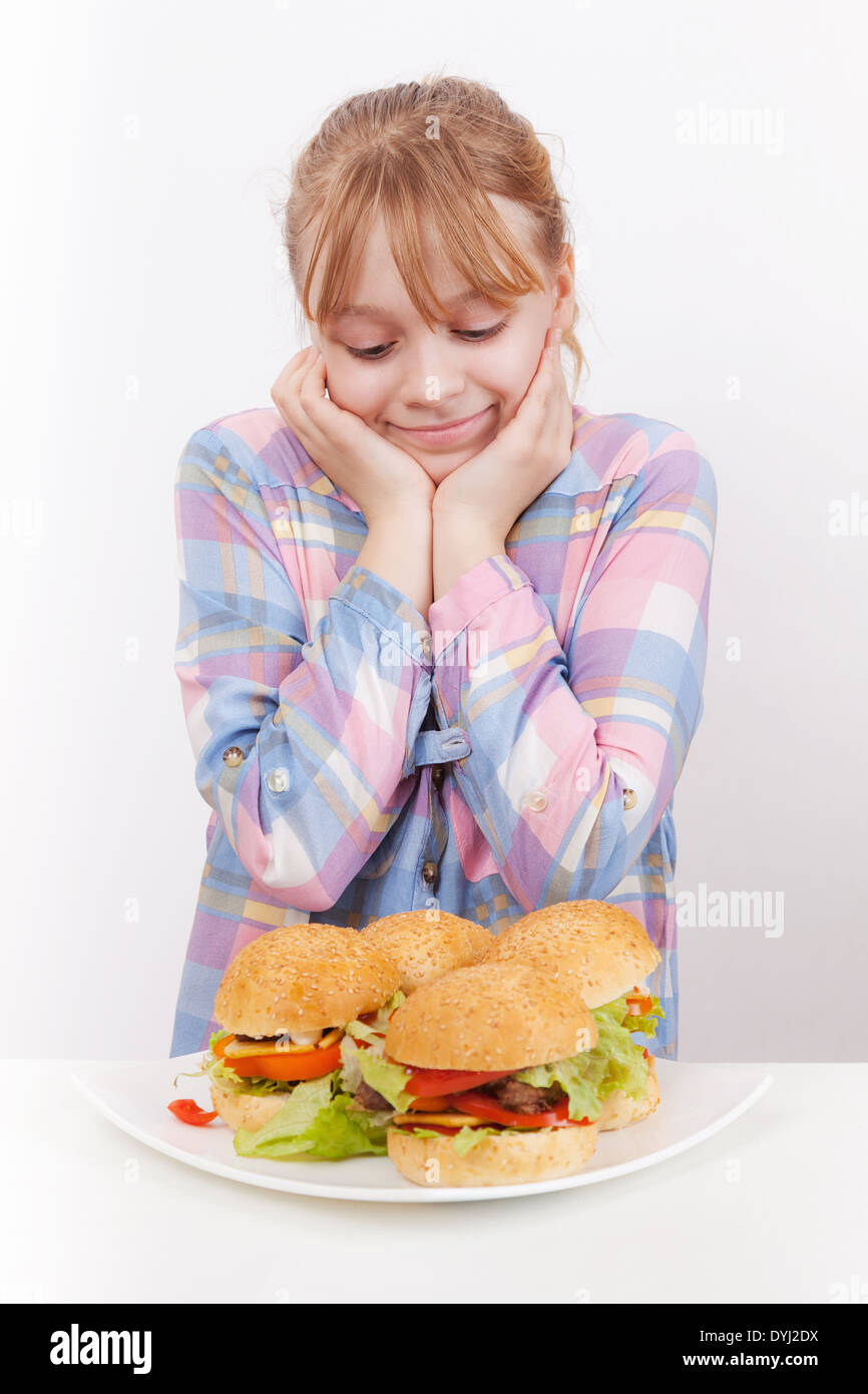 Poco sorridente ragazza bionda si affaccia su hamburger fatti in casa su piastra bianca Foto Stock