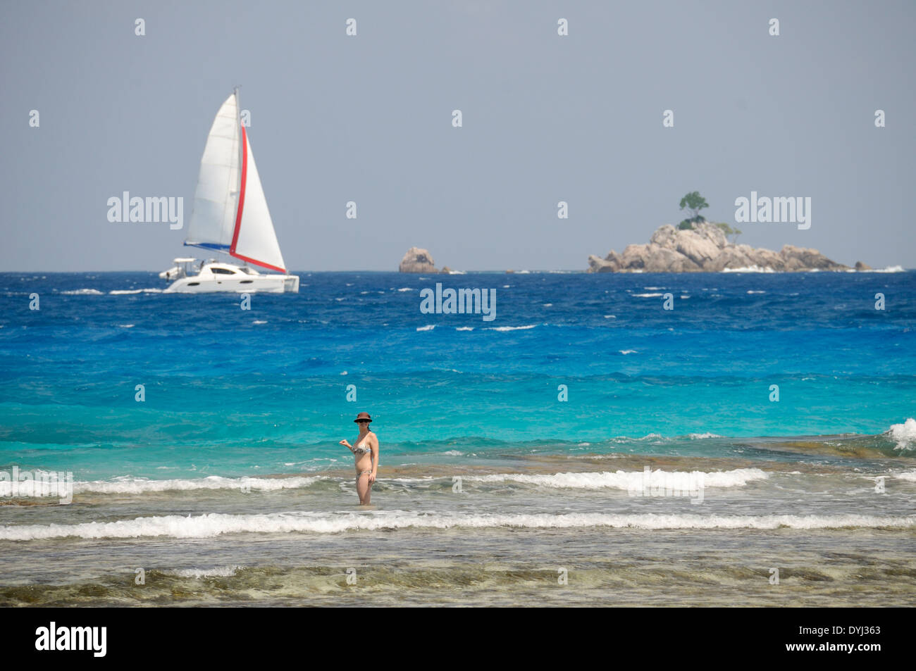 Barca a vela vista da anse Severe Beach con la donna sulla barriera corallina in primo piano a La Digue, Seicelle Foto Stock