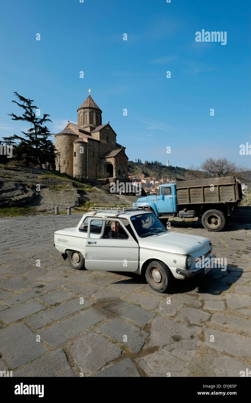 I vecchi veicoli parcheggiati al di sotto del quinto secolo Chiesa di Metekhi a Tbilisi, capitale della Repubblica di Georgia Foto Stock