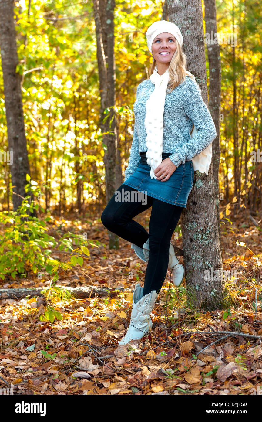39 anni di donna bionda che indossa un maglione, mini gonna e stivali passeggiate nel bosco in autunno. Foto Stock