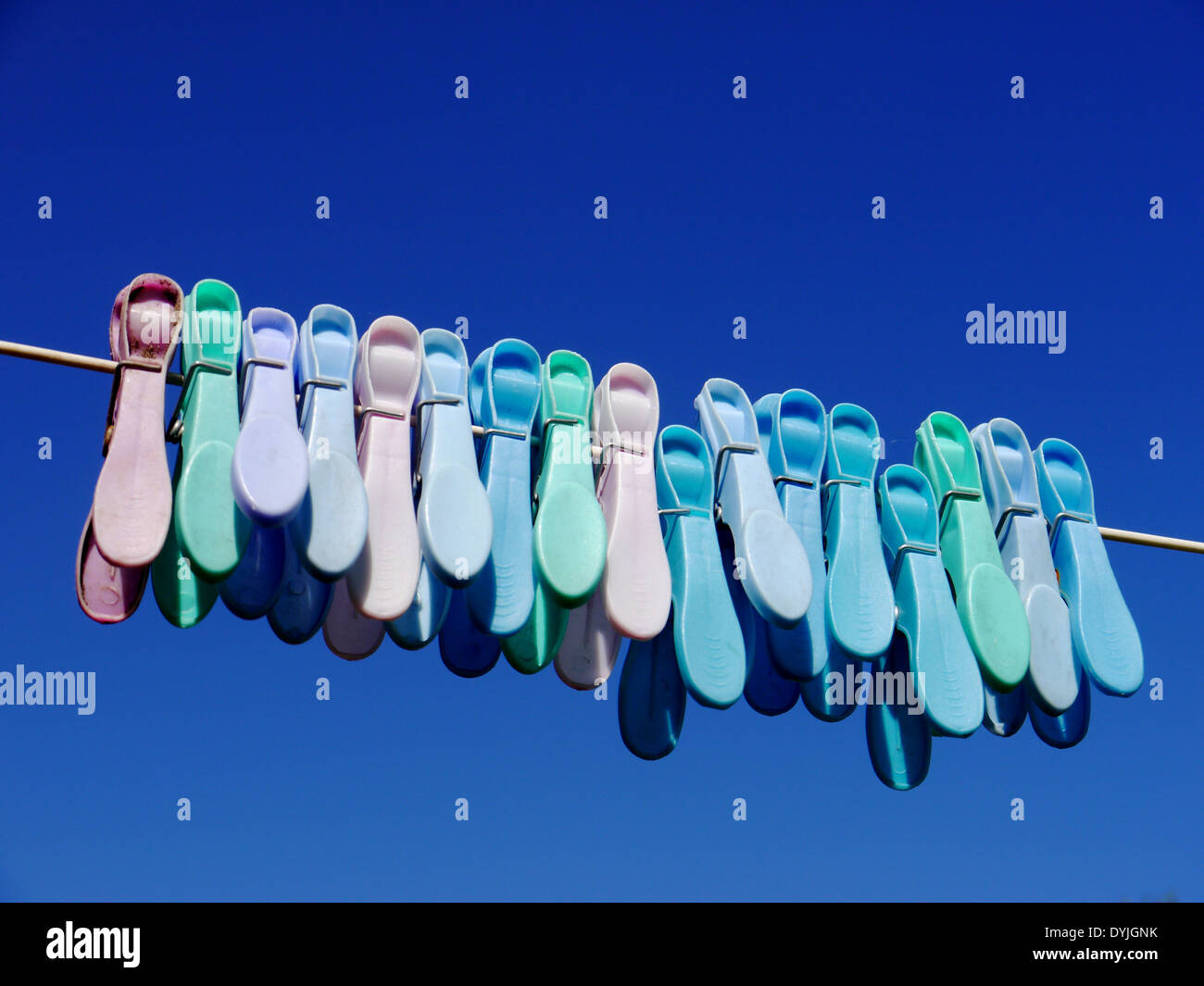 Immagine astratta che mostra in plastica colorata mollette su una linea di lavaggio, contro il luminoso cielo blu Foto Stock