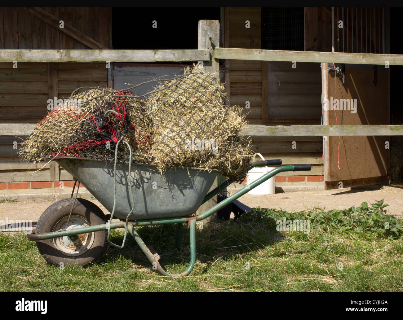 Carriola di tre sacchi di fieno reticolare / paglia per alimentazione di cavallo contro uno sfondo di maneggio, Foto Stock