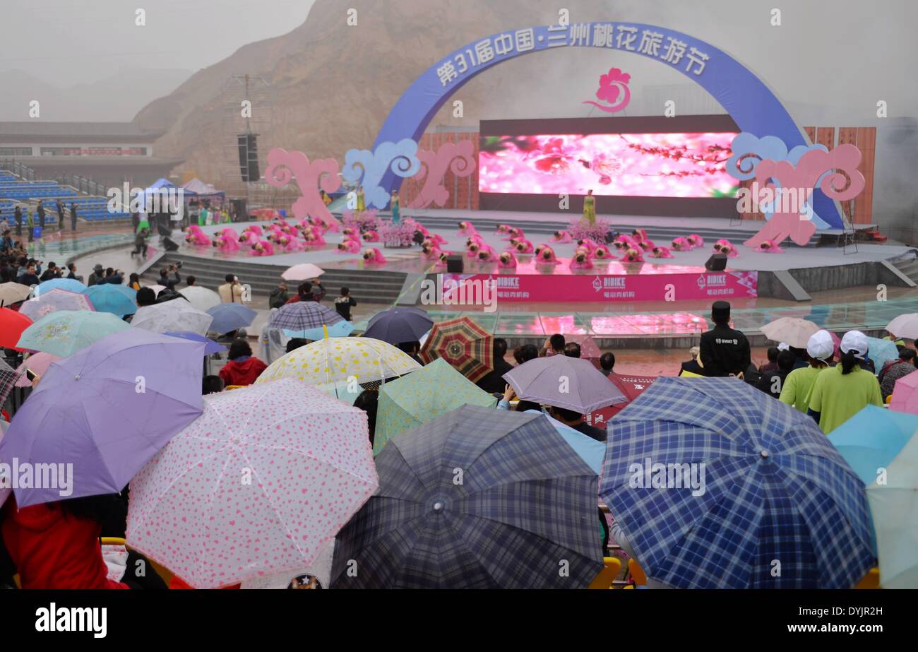 Lanzhou, la Cina della provincia di Gansu. Xx Apr, 2014. I residenti locali guarda le prestazioni in caso di pioggia durante la cerimonia di apertura del trentunesimo peach blossom festival del turismo a Lanzhou, capitale della Cina nord-occidentale della provincia di Gansu, 20 aprile 2014. Il festival, che è iniziata il giorno di Guyu (Grano pioggia), uno dei 24 termini solare creato da antichi cinesi per svolgere le attività agricole secondo la posizione del sole al cerchio zodiacale, durerà fino al mese di ottobre. © Chen Bin/Xinhua/Alamy Live News Foto Stock