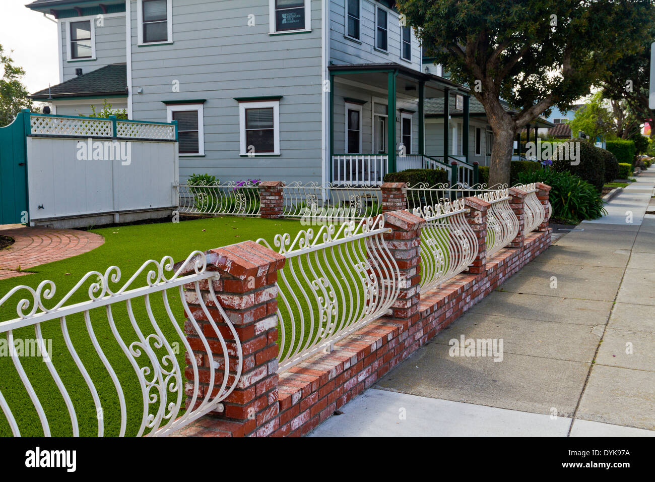 Interessante in mattoni rossi e verniciato di colore bianco in ferro battuto recinzione che circonda un cortile anteriore in Half Moon Bay, California Foto Stock