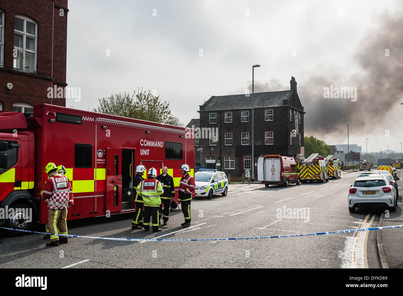 Leeds, West Yorkshire, Regno Unito, 21 aprile 2014. Una coltre di fumo si blocca in aria come i vigili del fuoco continuano ad affrontare un incendio in Leeds industrial estate. L'immagine mostra l'unità di comando su Armley Road. L'incendio scoppiato a circa 1,50 del mattino presso la sede di Tradpak un chimico di imballaggio e di impianto di riciclaggio nel Armley area della città. La fabbrica si trova vicino al centro della città e i residenti nelle vicinanze è stato detto di tenere le loro finestre e porte chiuse a causa delle sostanze chimiche potenzialmente tossiche implicate. Credito: Ian Wray/Alamy Live News Foto Stock