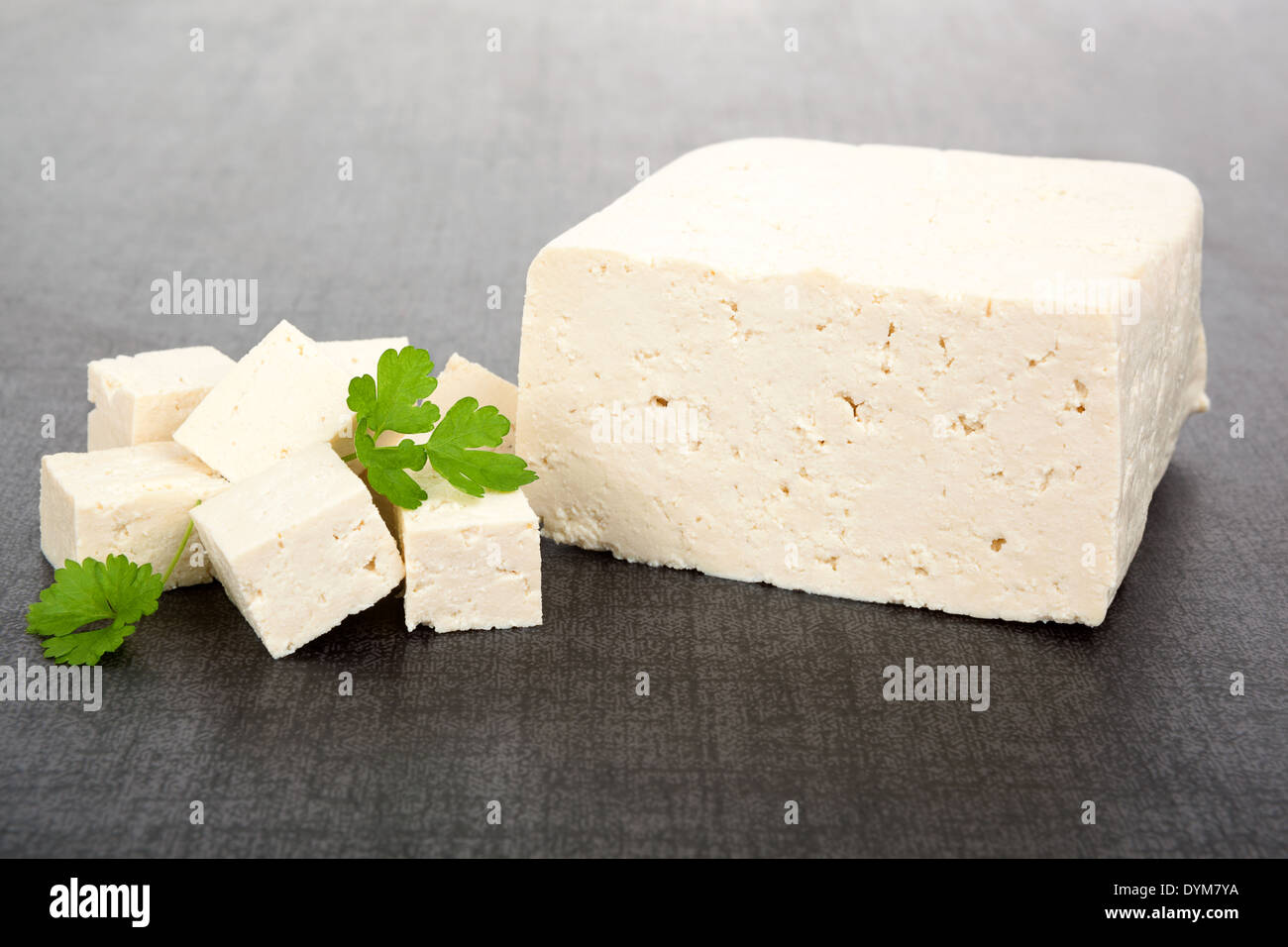 Lussuoso sfondo di tofu. Pezzo di tofu, cubi e prezzemolo fresco isolato su sfondo scuro. Delizie vegane e mangiare vegetariano Foto Stock
