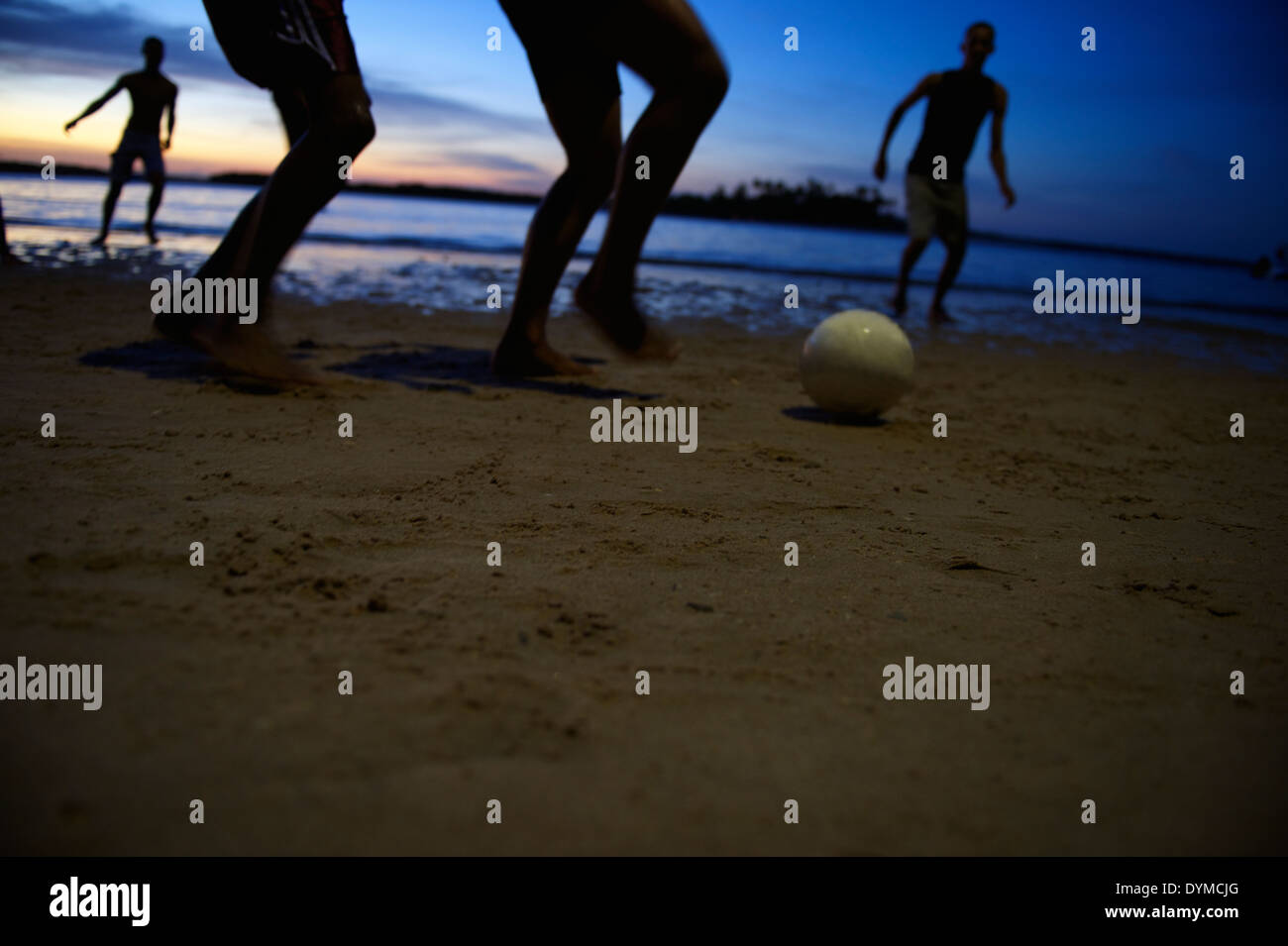 Il calcio brasiliano i giocatori di calcio in esecuzione durante la notte sulla spiaggia in una sfocatura di sagome ombra sulla riva di un fiume in Bahia Foto Stock