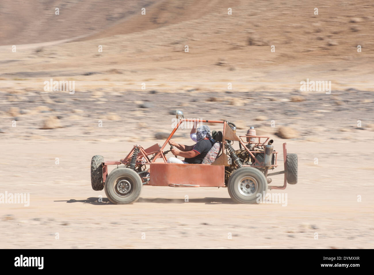 Uomo in un dune buggy racing attraverso il paesaggio del deserto in velocità con motion blur Foto Stock