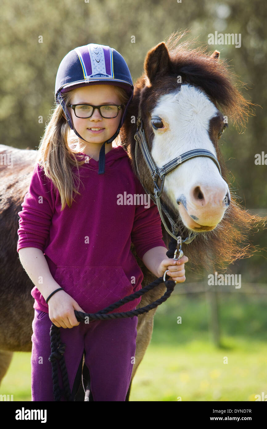 Una giovane ragazza in piedi con un pony al di fuori in campagna in una giornata di sole e sorridente alla fotocamera Foto Stock