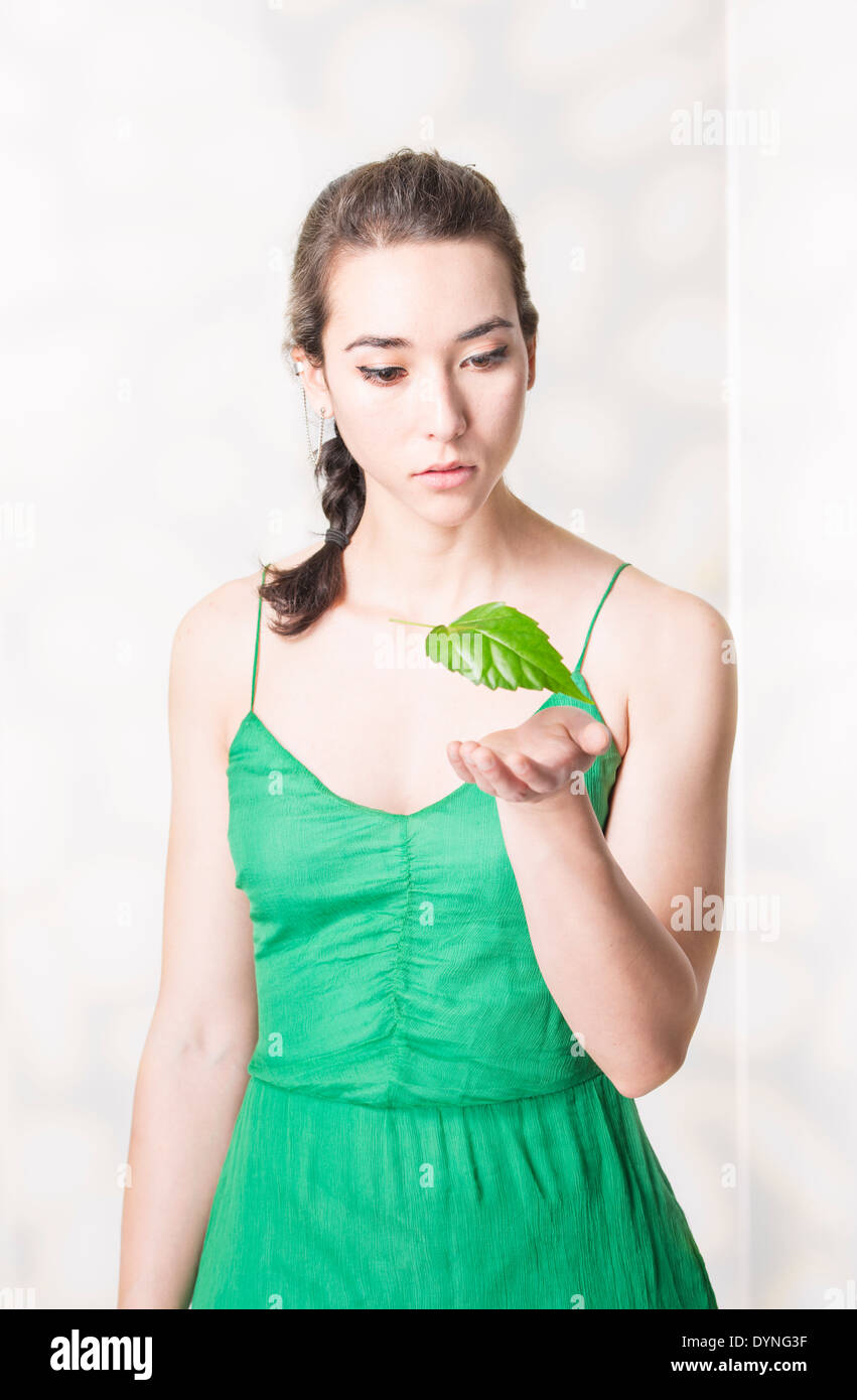 Donna che guarda stupito a foglia verde fluttuanti nell'aria. Immagine concettuale dell ambiente e la meraviglia della natura. Foto Stock