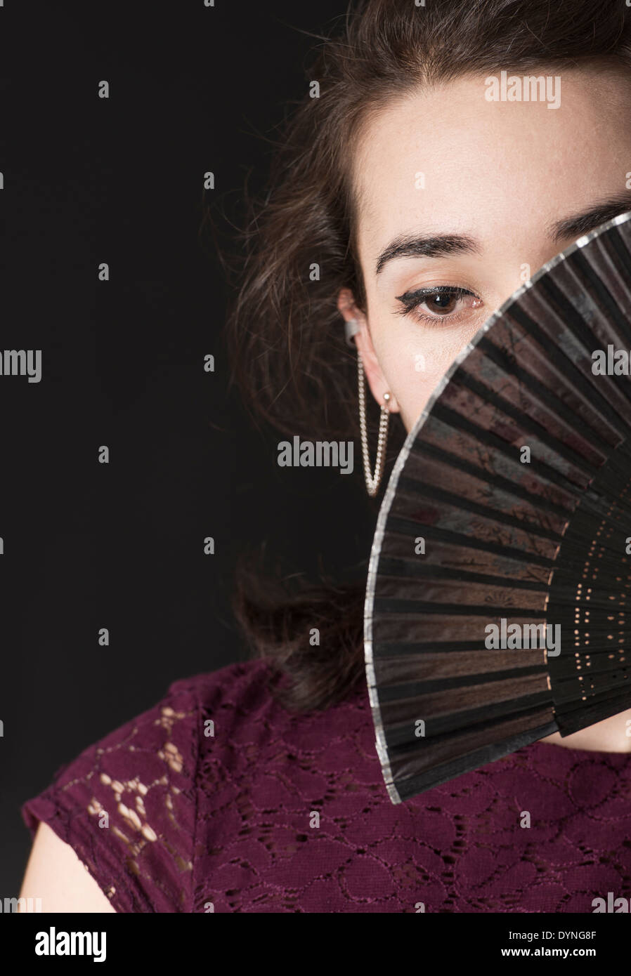 Malinconici donna ispanica che copre il volto con pieghevole la ventola a mano Foto Stock