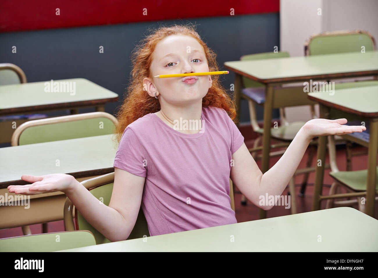 Ragazza fare sciocchezze nella scuola elementare di classe con una matita sopra le sue labbra Foto Stock