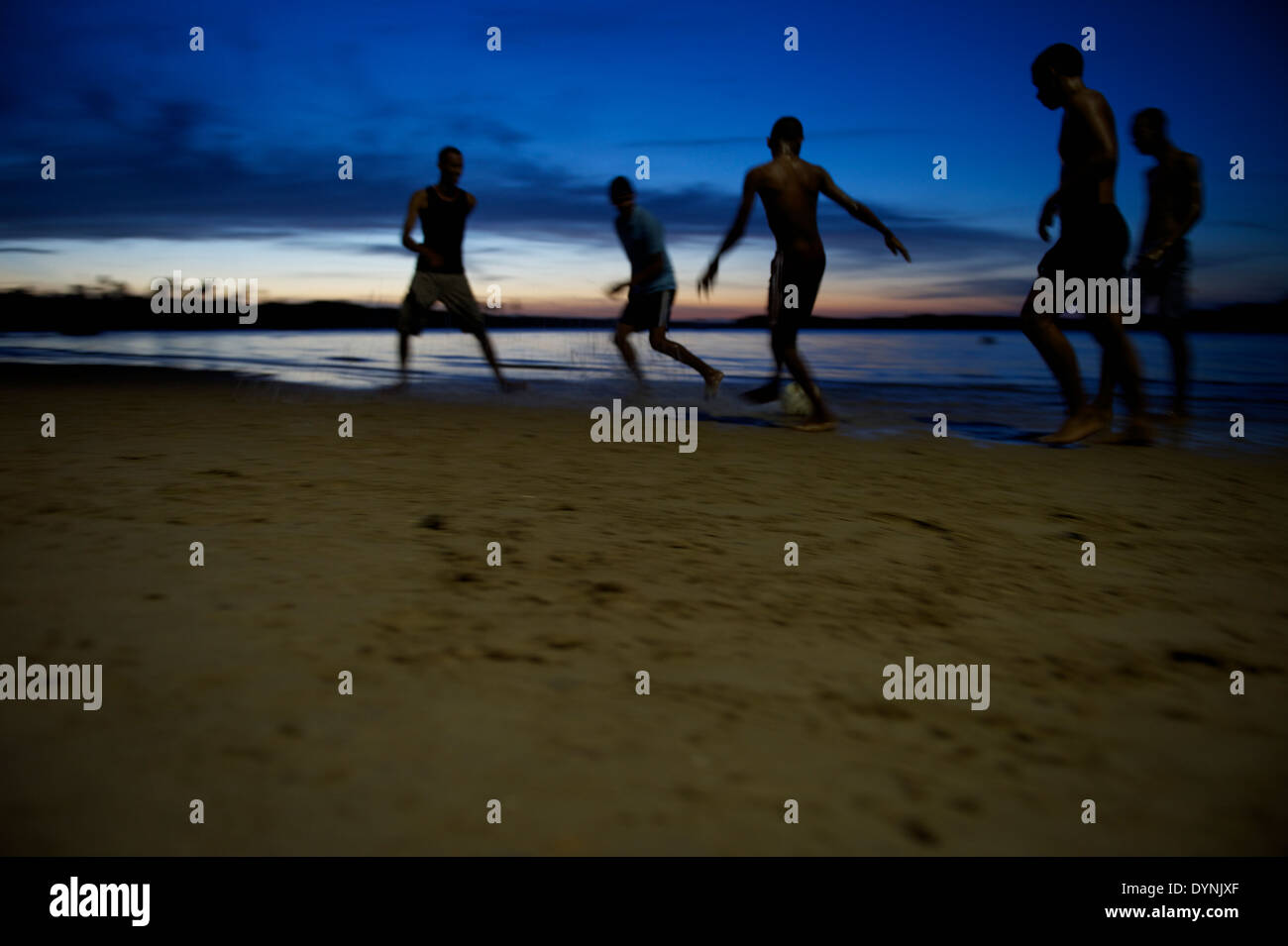 Il calcio brasiliano i giocatori di calcio in esecuzione durante la notte sulla spiaggia in blur di sagome ombra sulla riva di un fiume in Brasile Foto Stock
