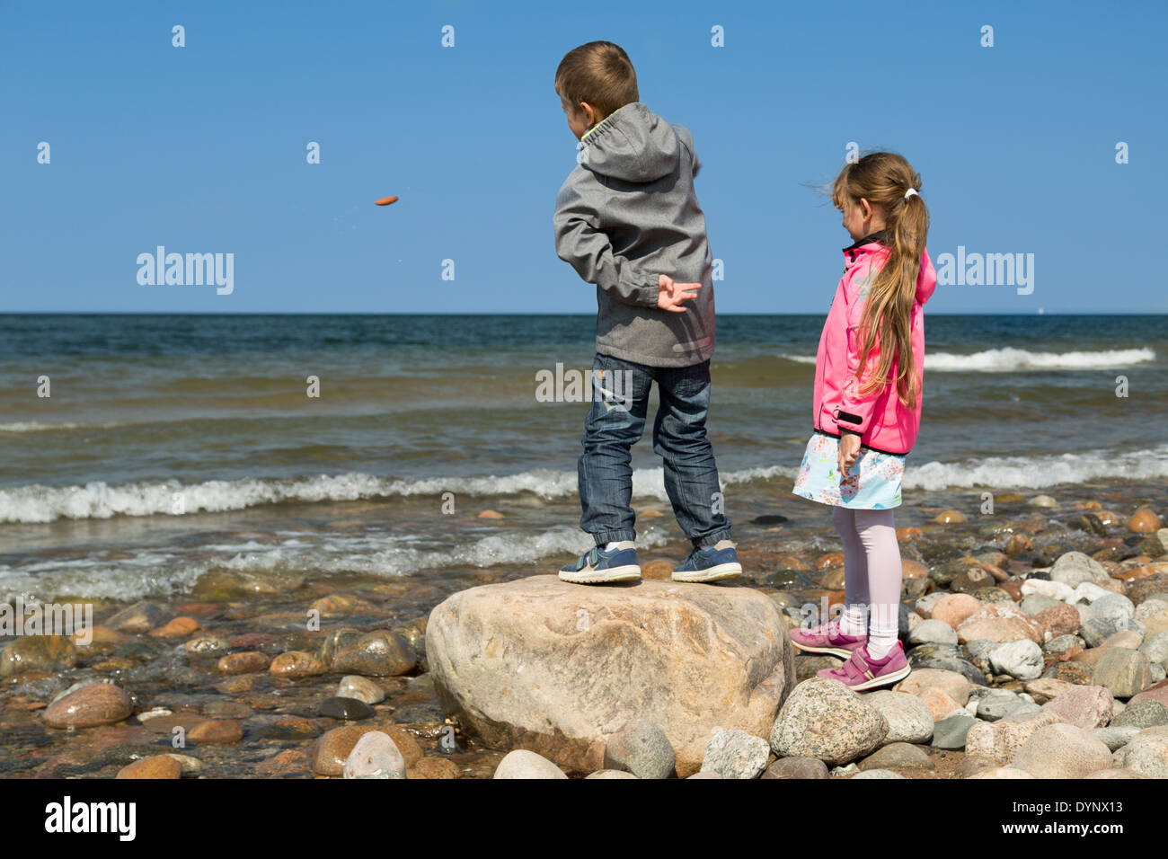 Un ragazzo e una ragazza lanciando rocce nell'oceano. Foto Stock