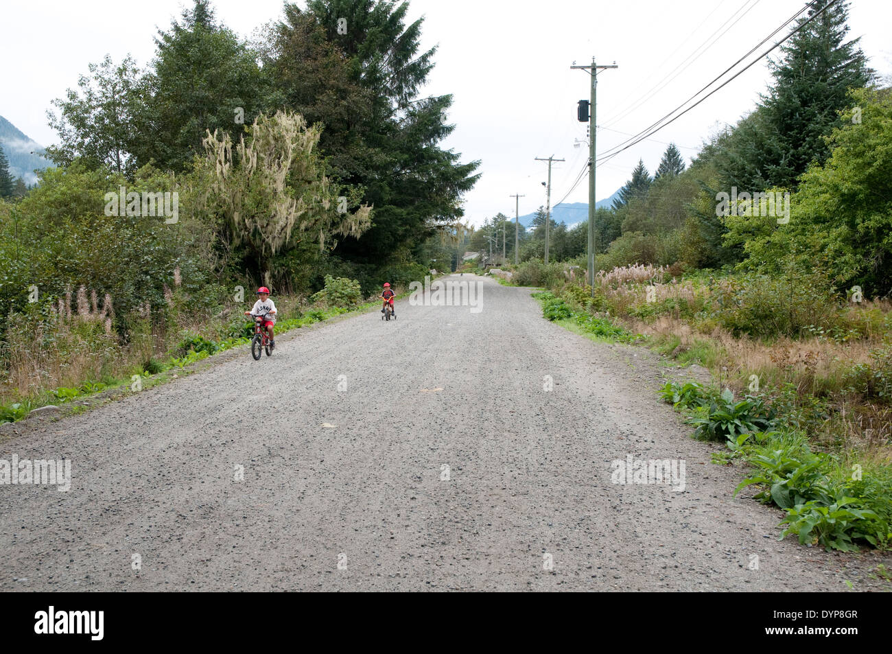 Due giovani ragazzi guidare le loro biciclette su prenotazione nativo di Wuikinuxv, nel grande orso nella foresta pluviale, British Columbia, Canada. Foto Stock