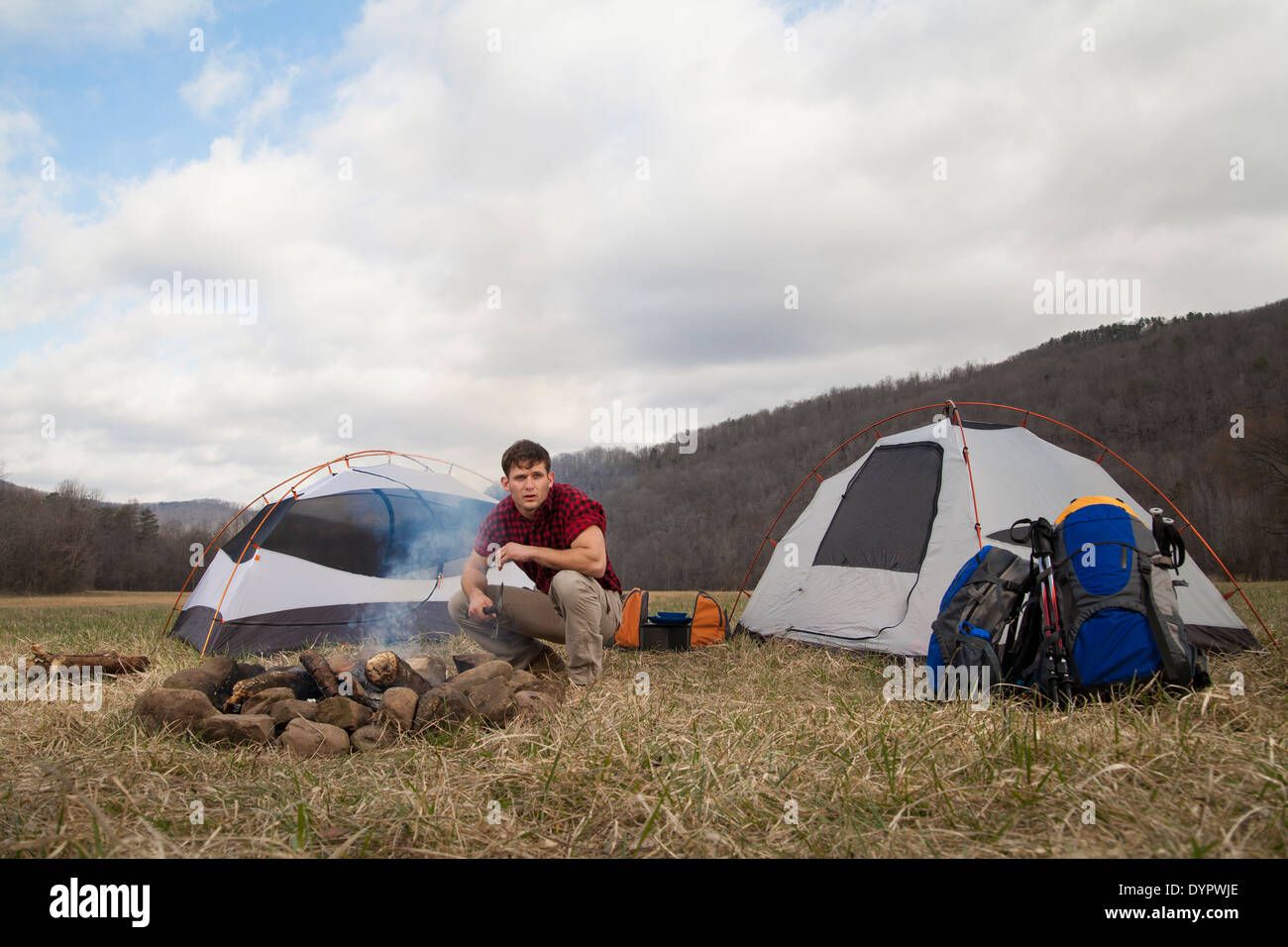 Maschio caucasico si divide in legno e rende il fuoco di campo accanto alla tenda Foto Stock