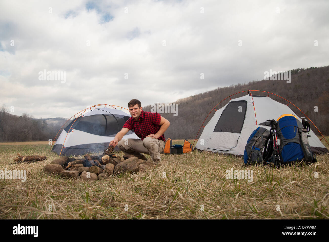 Maschio caucasico si divide in legno e rende il fuoco di campo accanto alla tenda Foto Stock