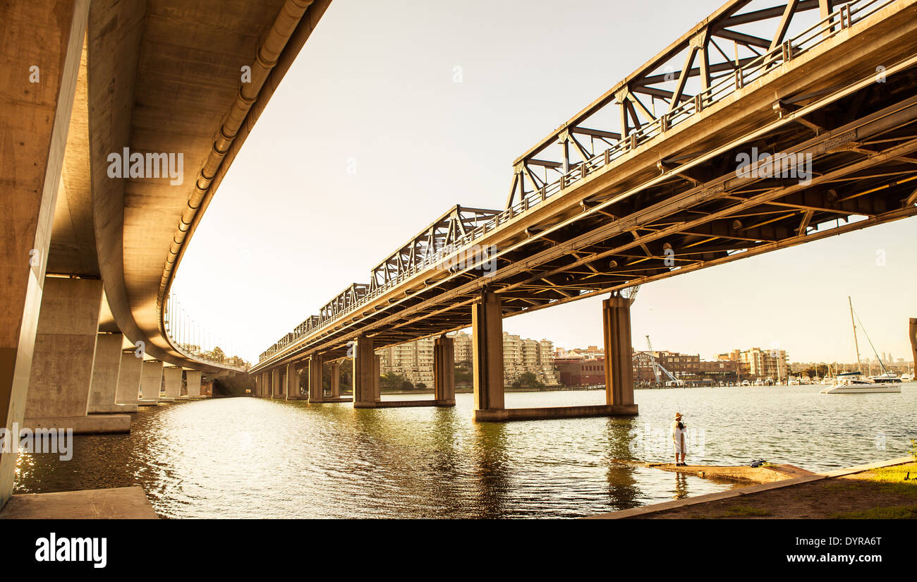 Un ferro vecchio ponte stradale accanto a un moderno uno a Sydney con un uomo la pesca a distanza Foto Stock