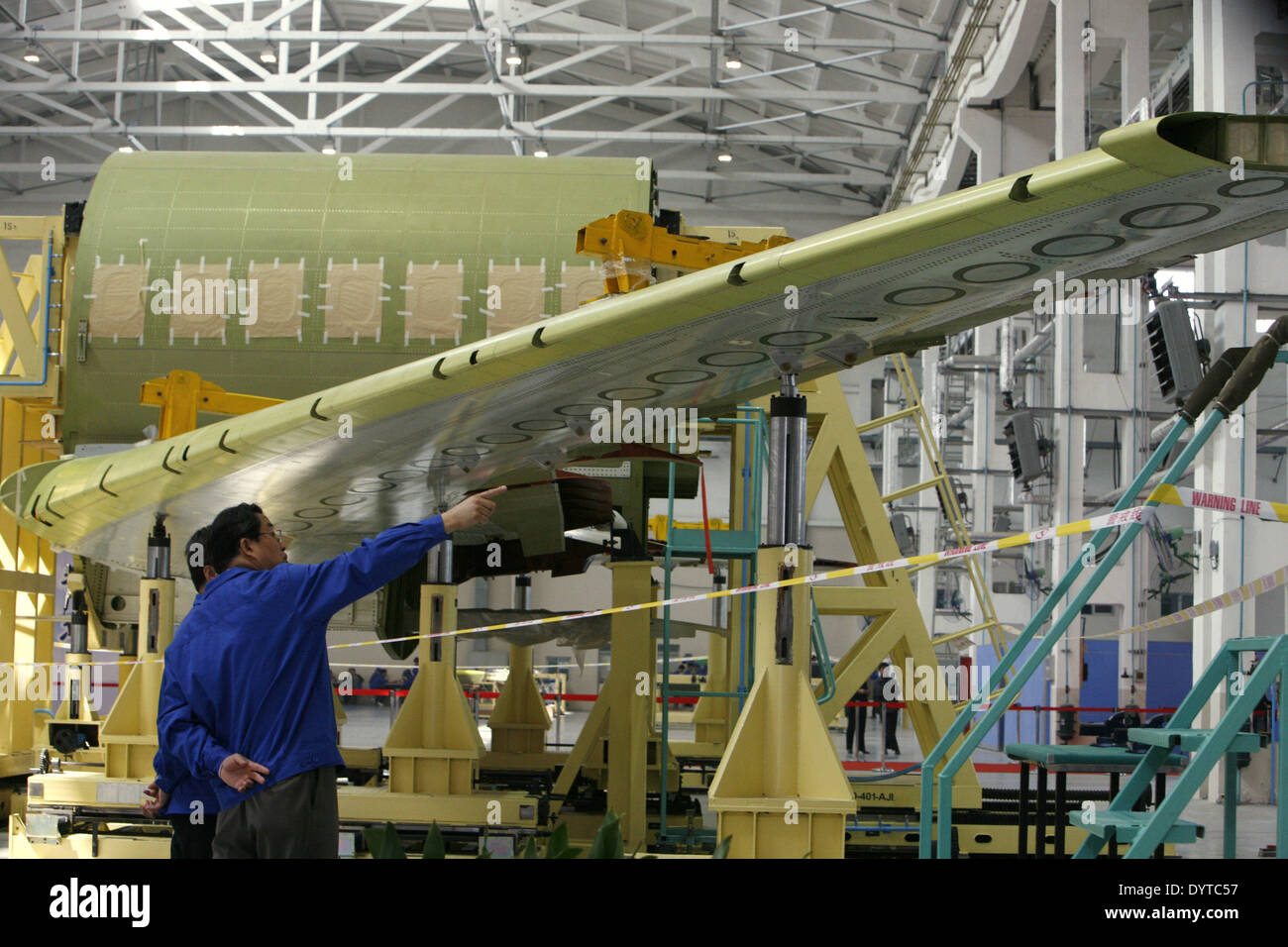 2 lavoratori cinesi discutere davanti a un'ala parte di ARJ 21 aeromobili commerciali in corrispondenza di una linea di assemblaggio durante una cerimonia di gruppo Foto Stock