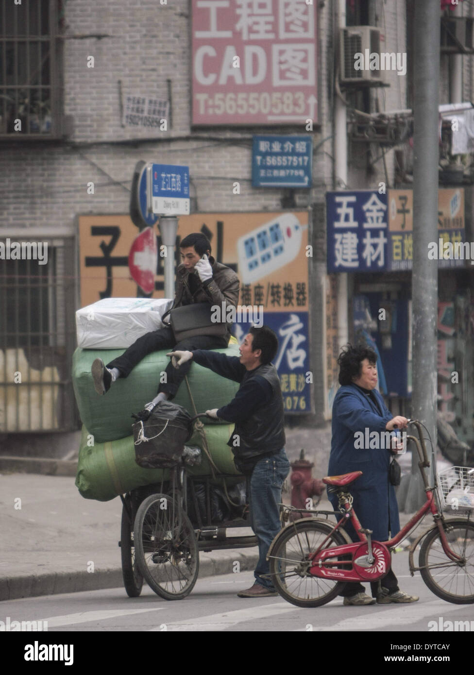Un triciclo cale di driver a pieno carico di merci e un cliente su una strada Foto Stock