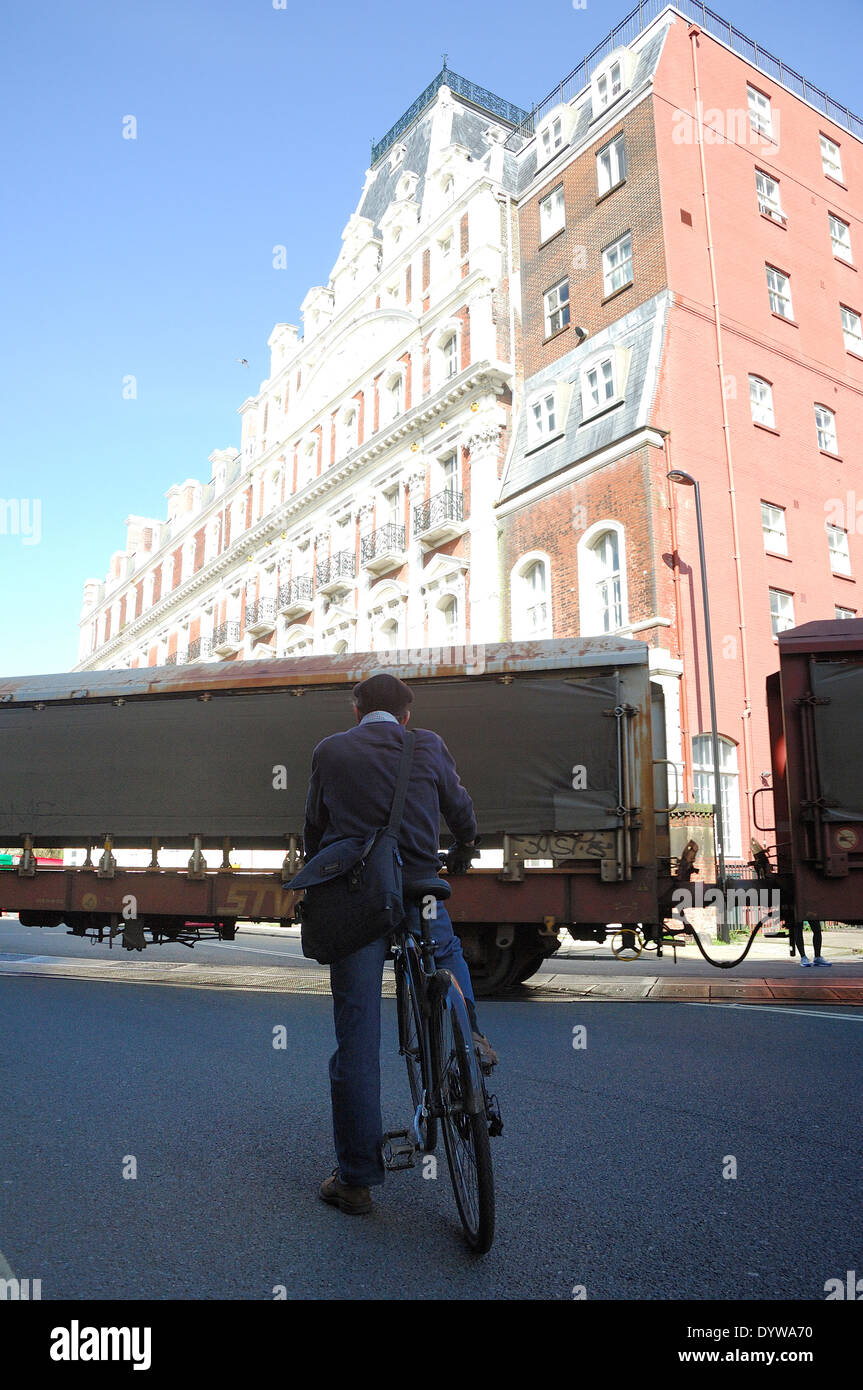 Ciclista vi attende sulla strada per treno merci per passare da a Southampton Foto Stock