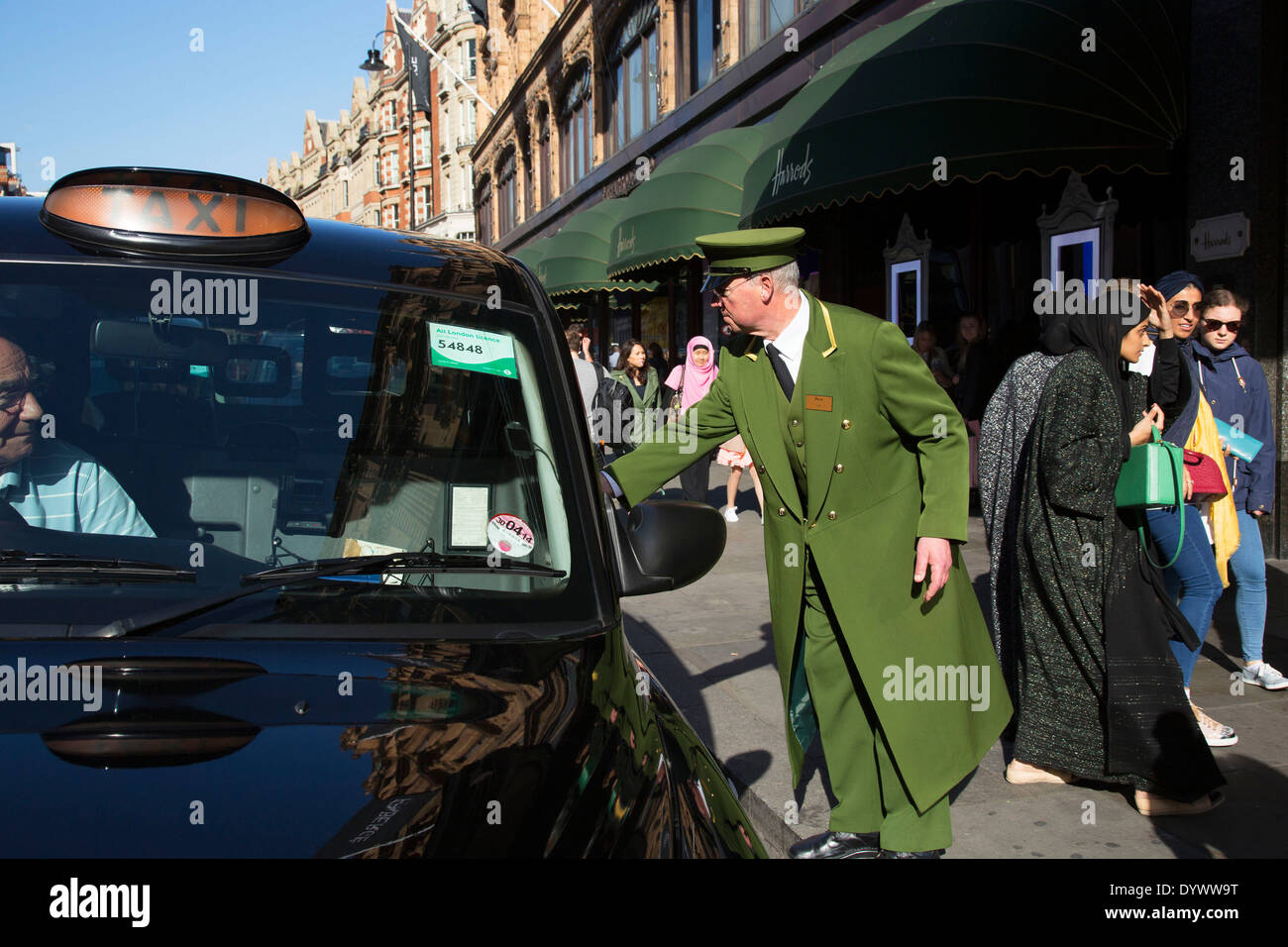 Portiere assiste gli acquirenti di arrivare in taxi fuori i grandi magazzini Harrods nella esclusiva area di Knightsbridge. Londra, Regno Unito. Foto Stock