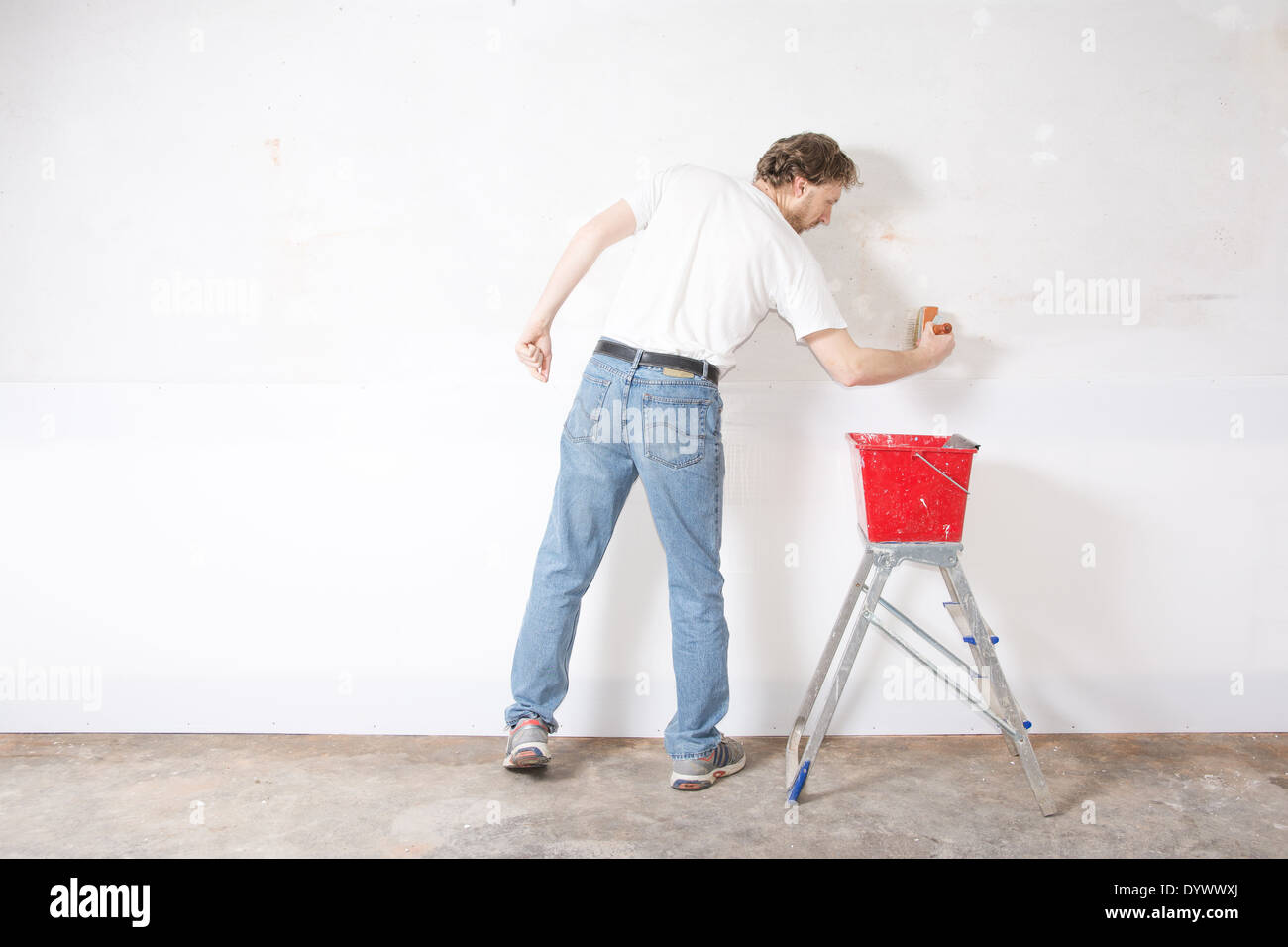 L'uomo pittura un muro bianco con spazzola di vernice Foto Stock