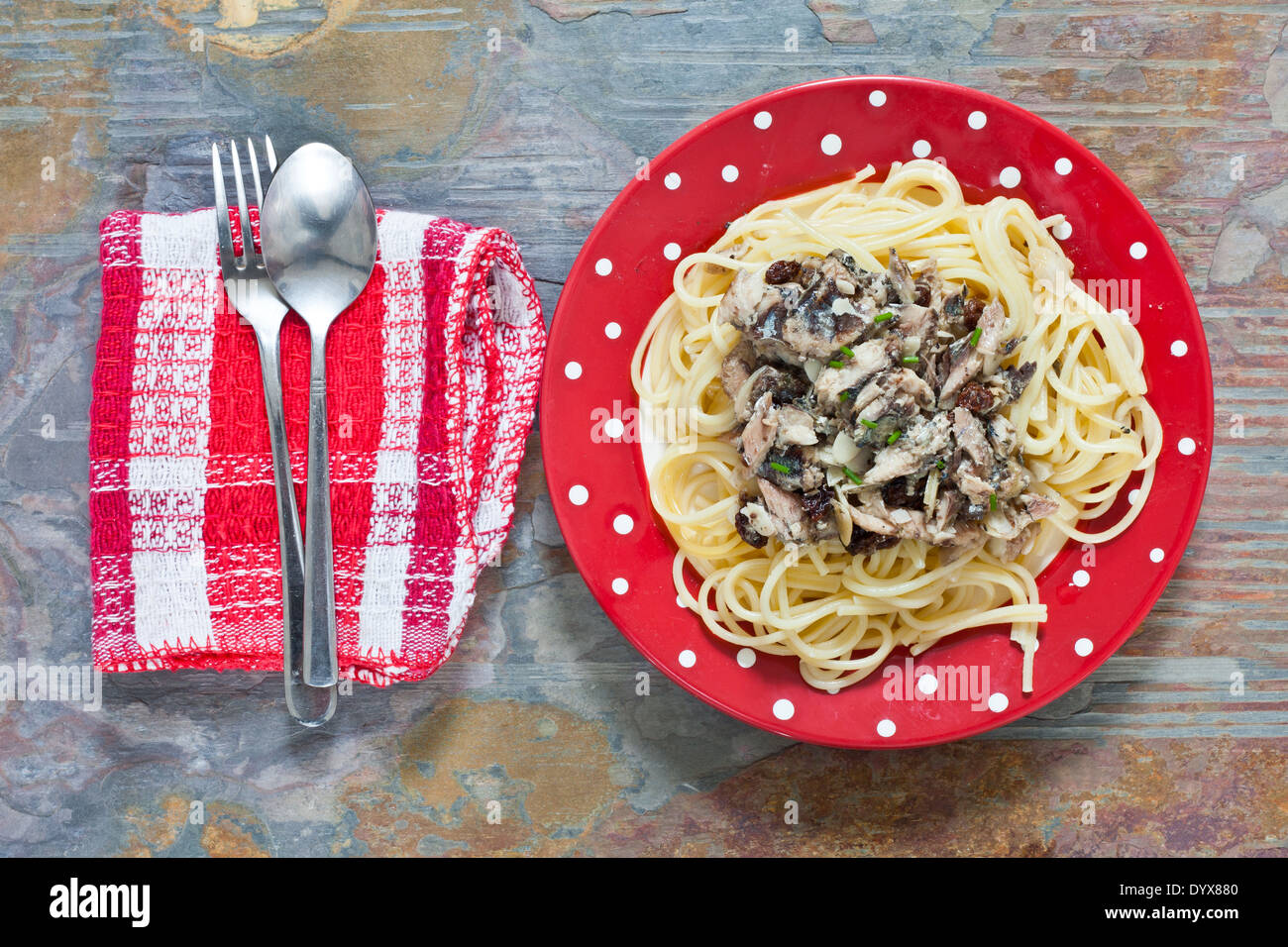 Sardine e uvetta con spaghetti su una targhetta rossa su un tavolo di pietra Foto Stock