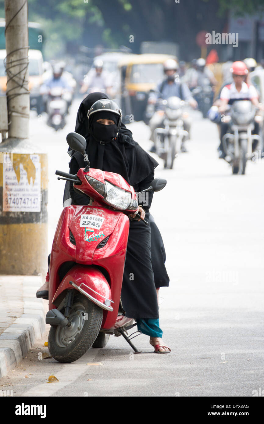 Un elegante donna che indossa un velo niqab, seduta sul suo scooter con un amico mentre guardando freddamente nella fotocamera. Foto Stock